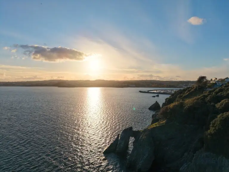 Drone image of sunset taken from over the sea showing coastline and harbor in the distance.